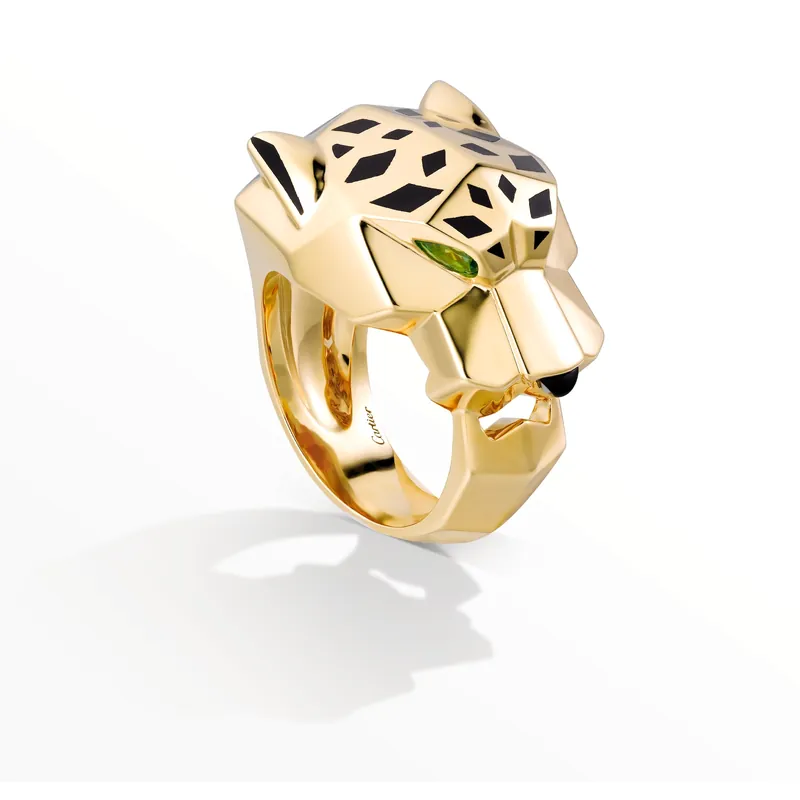 Panthère de Cartier ring in yellow gold: a sculpted panther head with black lacquer spots, green eyes and an onyx nose, on a pale grey ground.