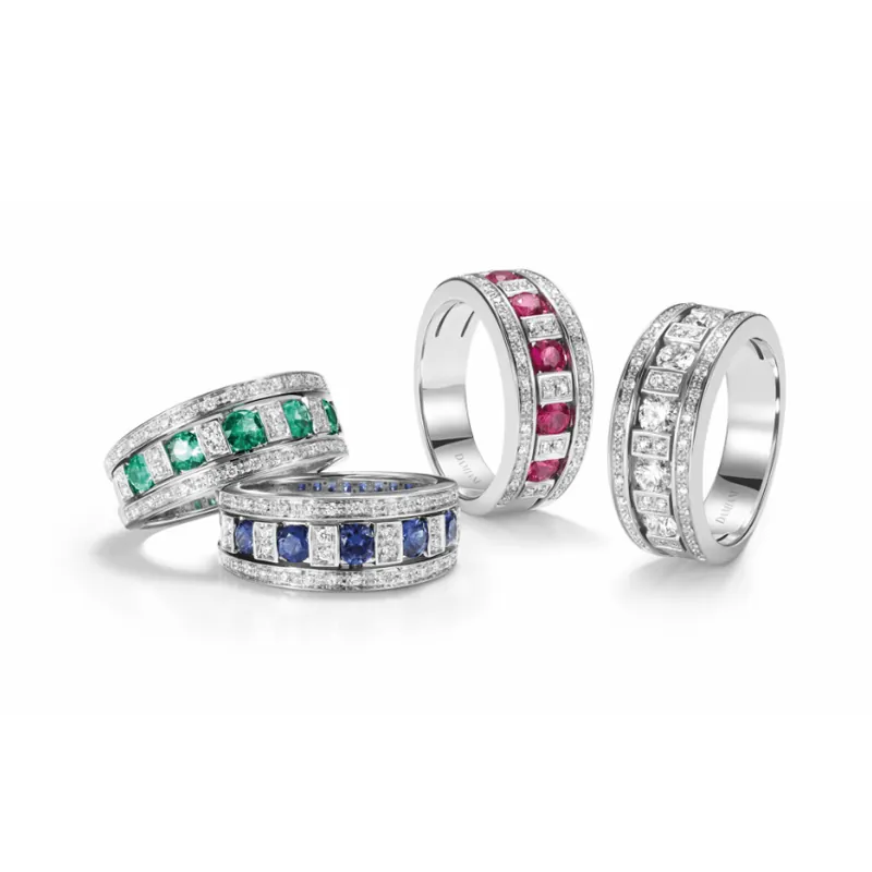 Four Belle Époque band rings in white gold, set with emeralds, sapphires, rubies and diamonds alternating with diamonds, grouped at the left of a wide white banner