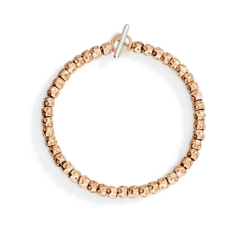 Granelli bracelet: a circle of dimpled rose-gold grains closed by a white-metal T-bar, on a white ground
