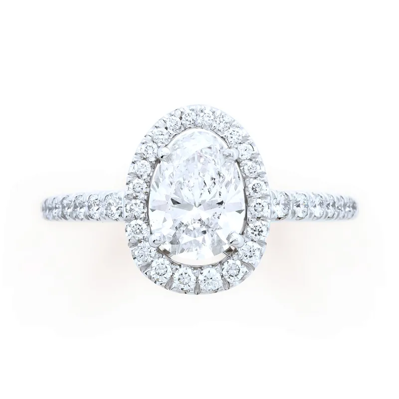 Mellerio Cut ring in white gold: an oval-shaped diamond in a halo of small diamonds on a pavé band, seen from above on a cream ground