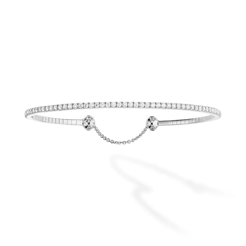 Skinny rivière bracelet in white gold: a thin flexible line of diamonds forming a bangle, with a fine safety chain, on a pale grey ground.