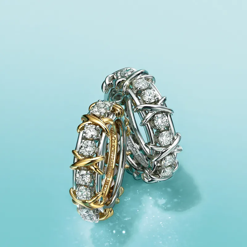 Two Jean Schlumberger Sixteen Stone rings, one in 18k yellow gold and platinum and one in platinum, round diamonds held by small crossed Xs, on a Tiffany Blue ground.