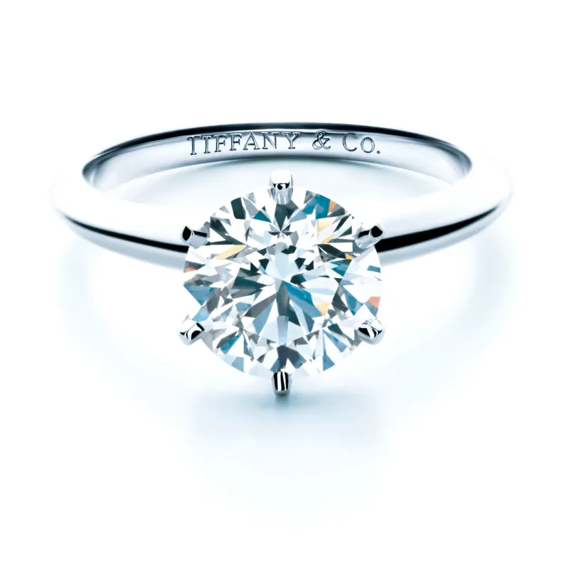 The Tiffany Setting engagement ring: a round brilliant diamond held by six prongs on a platinum band engraved Tiffany & Co., on a white ground.